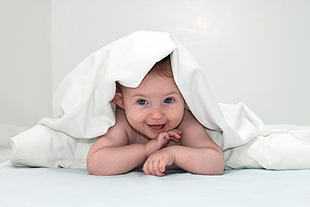 baby showing face under white blanker